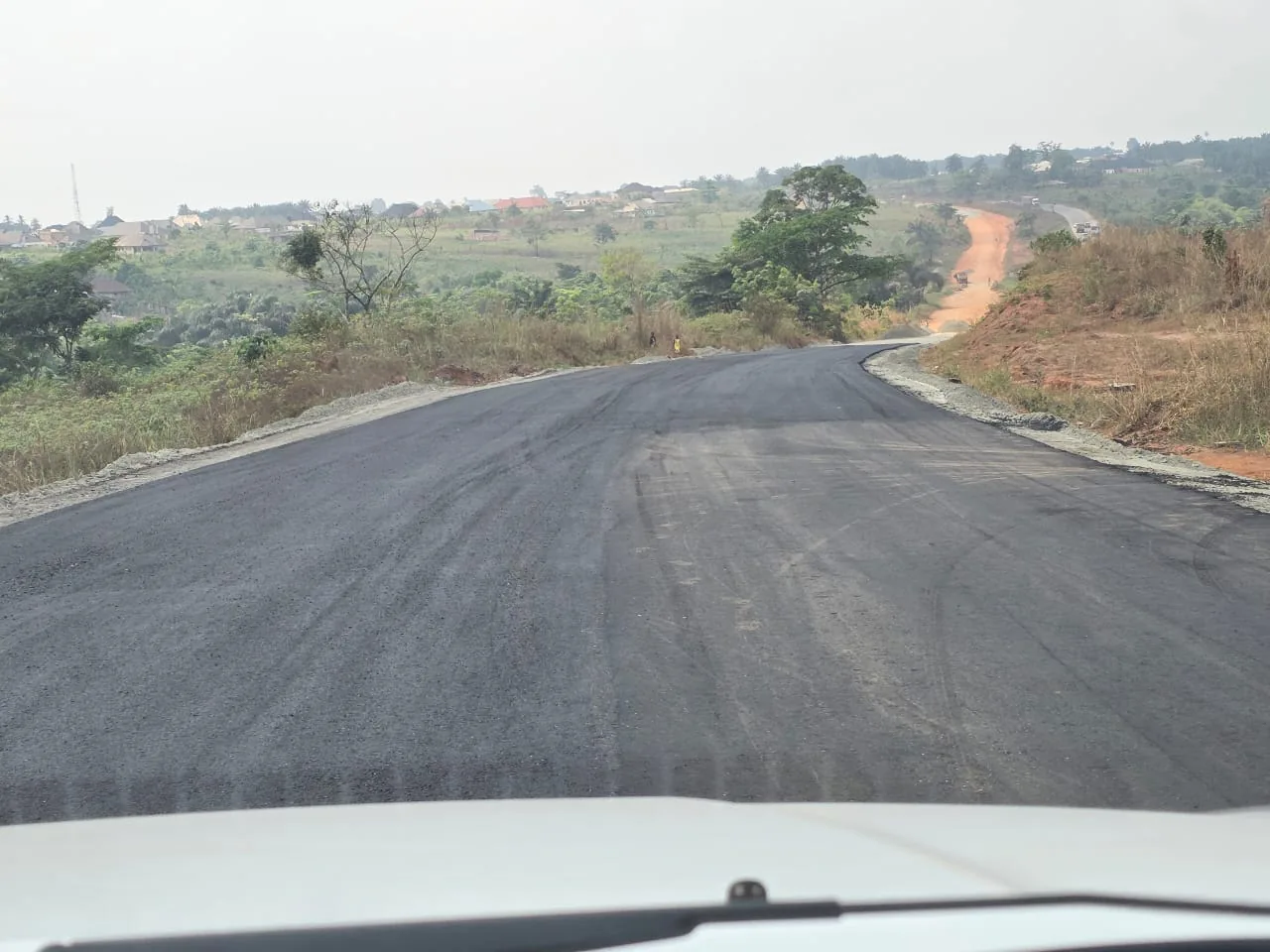 Newly laid asphalt running over rolling terrain, seen from a vehicle travelling along the corridor.