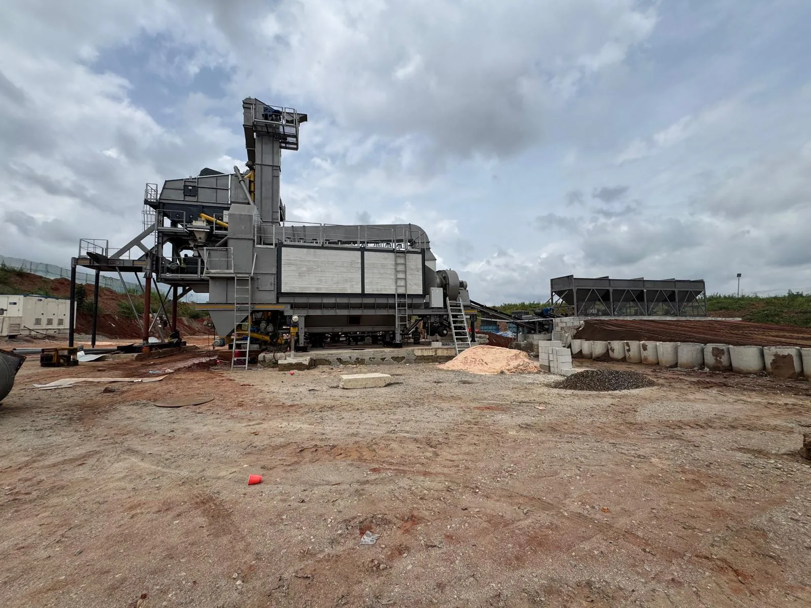 An asphalt mixing plant erected on a cleared site, with conveyor, mixing tower and cold-feed bins.