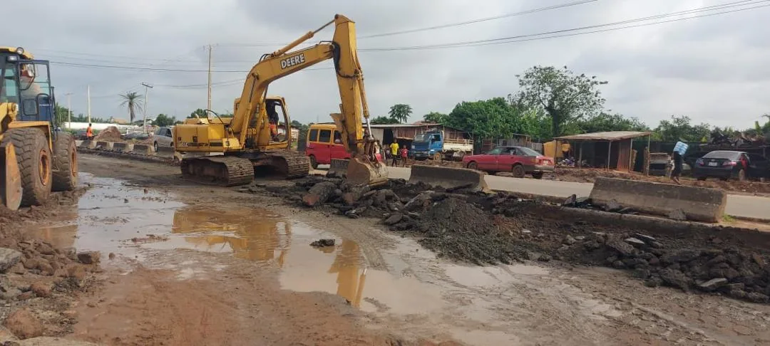 Excavators breaking out the old road surface beside a concrete barrier, with traffic running on the adjacent carriageway.
